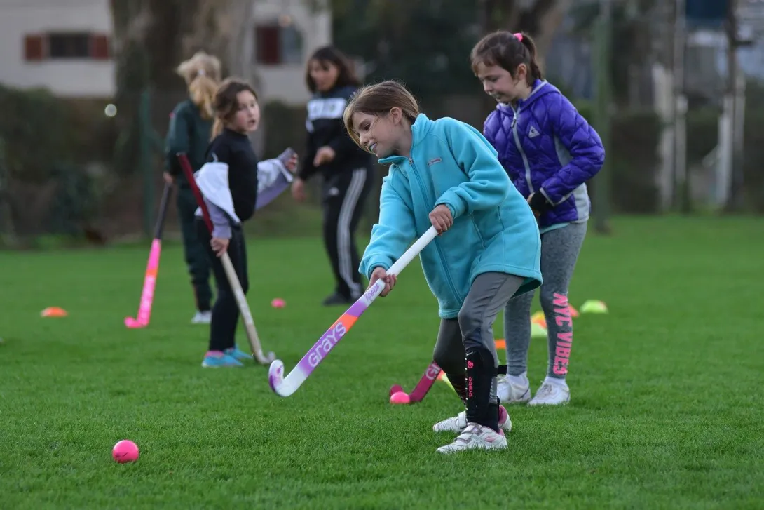 Niñas practicando conducción de pelota con palos de hockey en el césped del Club