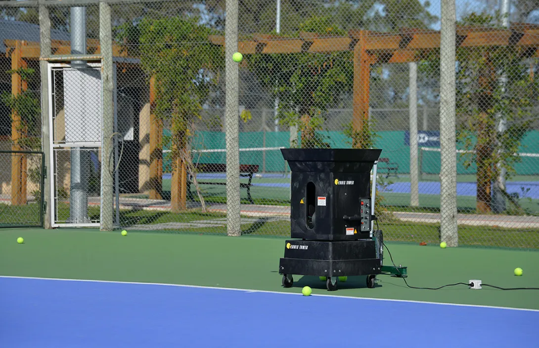 Máquina lanza pelotas en funcionamiento sobre una cancha de tenis de la Sede Solymar