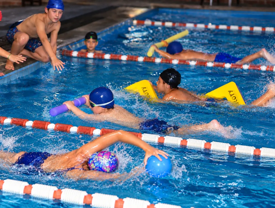 Niñas y niños realizan ejercicios con flotadores en una piscina del Club